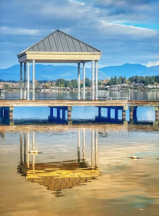 A covered gazebo at the end of a dock on Lake Stevens, mirrored in calm water.